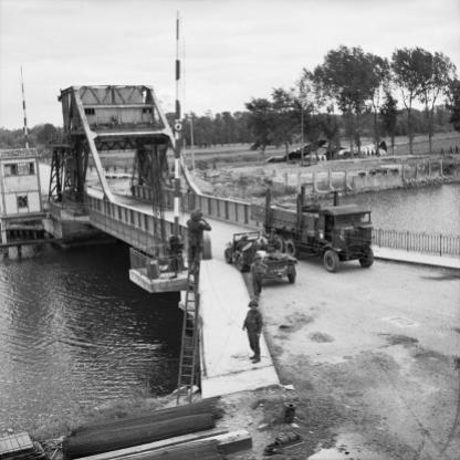 Pegasus Bridge, 9 June 1944. Vehicles including a Royal Signals jeep & trailer and a RASC Leyland lorry on 'Pegasus Bridge' over the Caen Canal at Benouville. The signallers are fixing telephone lines across the bridge. Photograph: Sergeant Christie. No. 5 Army Film and Photo Section, Army Film and Photographic Unit Imperial War Museum Catalogue Number: B 5288