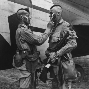 Paratroopers Clarence C. Ware and Charles R. Plaudo from HQ Co. 506 PIR. 101 Abn Div, painting each other's faces on the afternoon of June 5, 1944. This phot was printed in Stars and Stripes, and helped form the legend of "The Filthy Thirteen. US National Archives Accession Number: 111-SC-193551